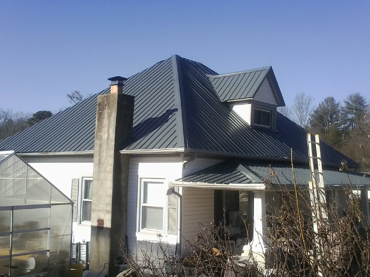 Dark blue standing seam metal roof on a white farmhouse with dormer — Slate & Tile Roof Repair by Roofing Brothers in Orange City